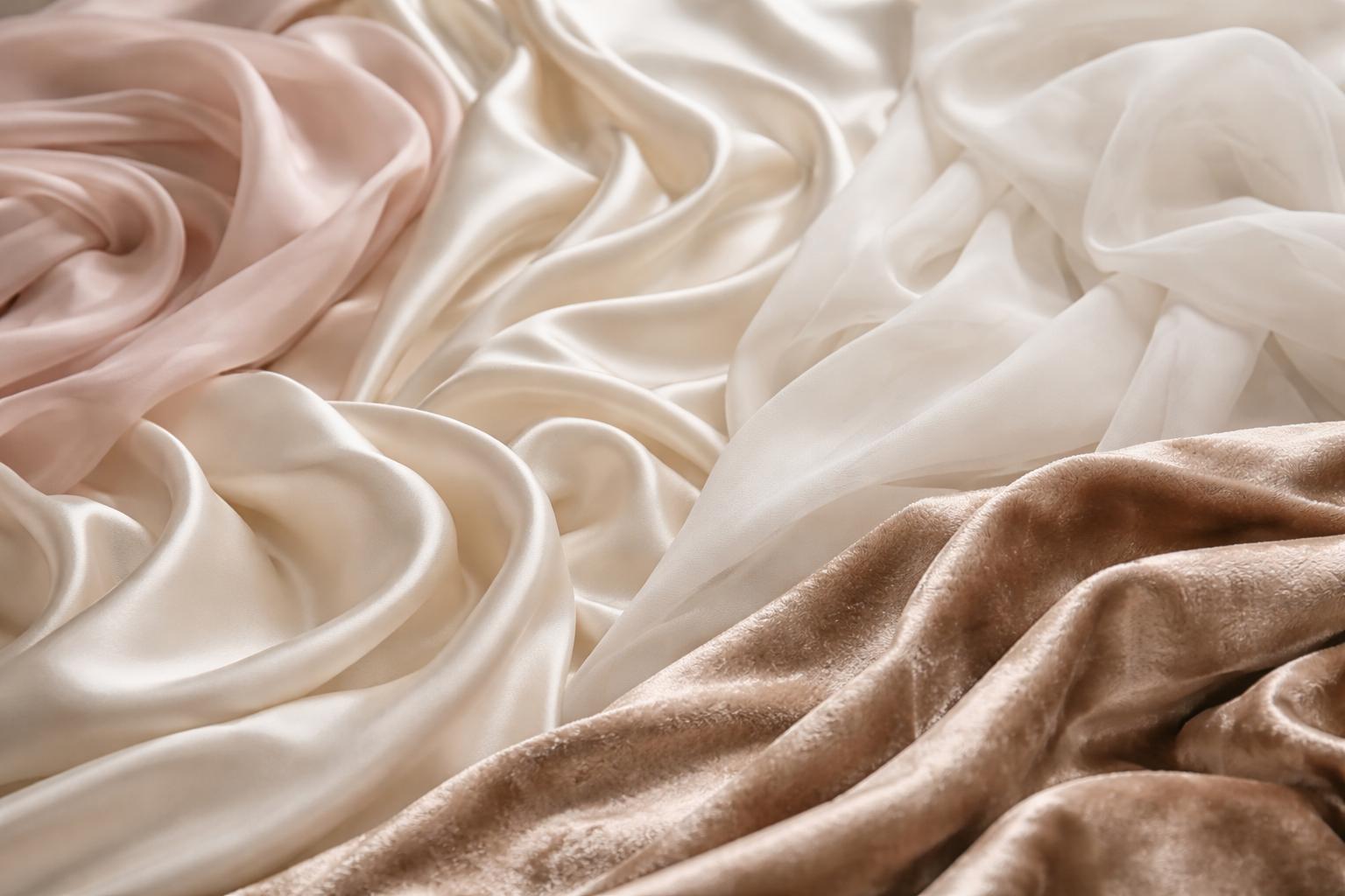 Gros plan de différents tissus en soie — satin duchesse, crêpe de Chine, mousseline et velours — aux tons ivoire et poudrés, illustrant le savoir-faire couture de Maison Galad